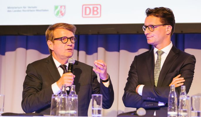 DB-Vorstandsmitglied Ronald Pofalla und NRW-Verkehrsminister Hendrik Wüst reden auf der Bühne.