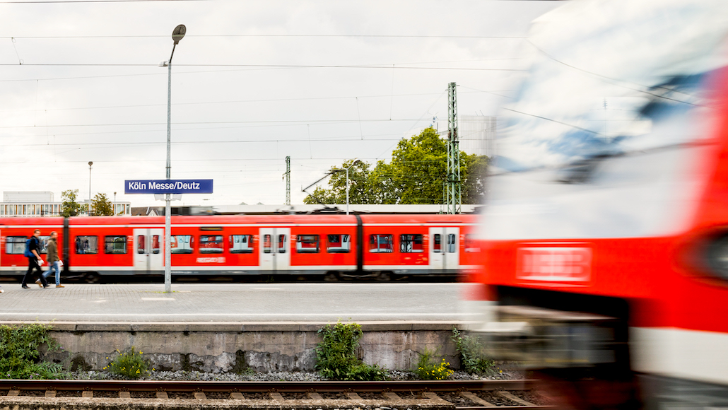 Ein Foto des Bahnsteiges Köln Messe / Deutz. Im Vordergrund fährt gerade ein Zug ein.
